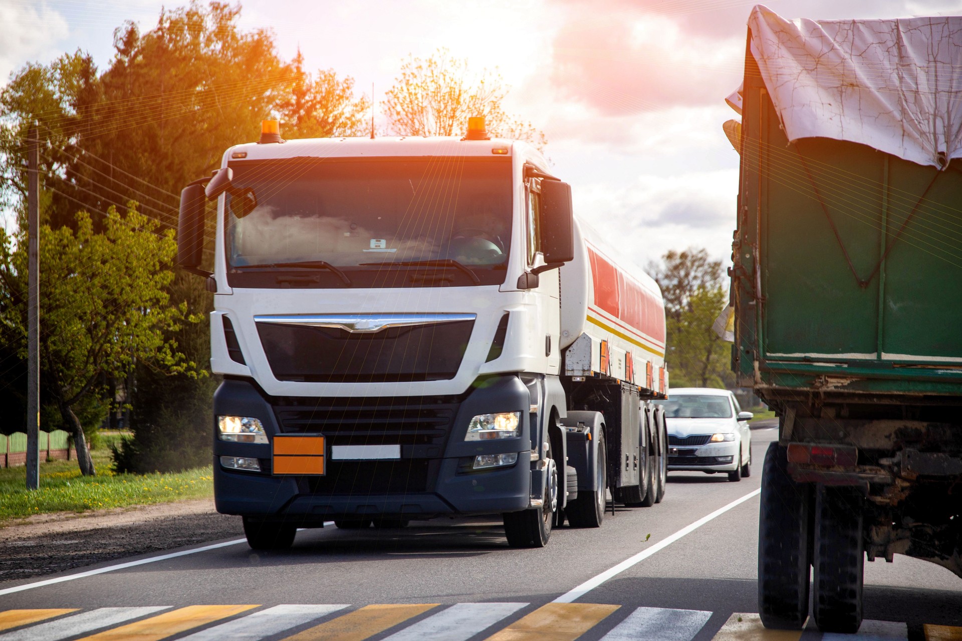 Modern truck with tank trailer transports dangerous cargo acetone and oil against cloudy sky and sun, industry. Fire hazard class